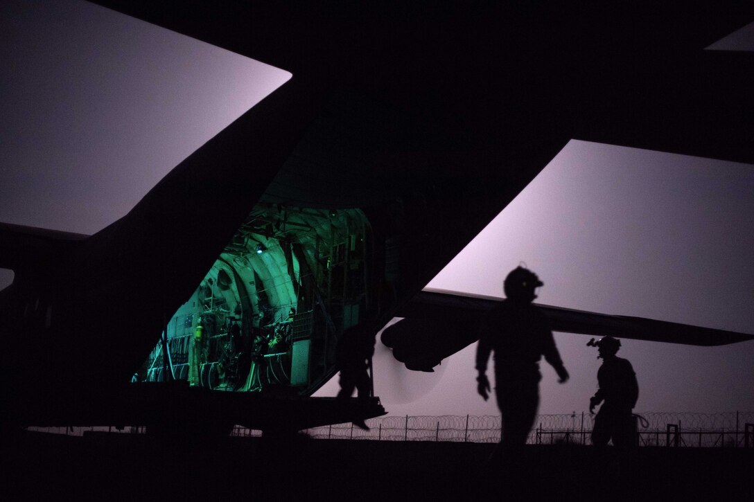 Airmen walk behind an opened aircraft.