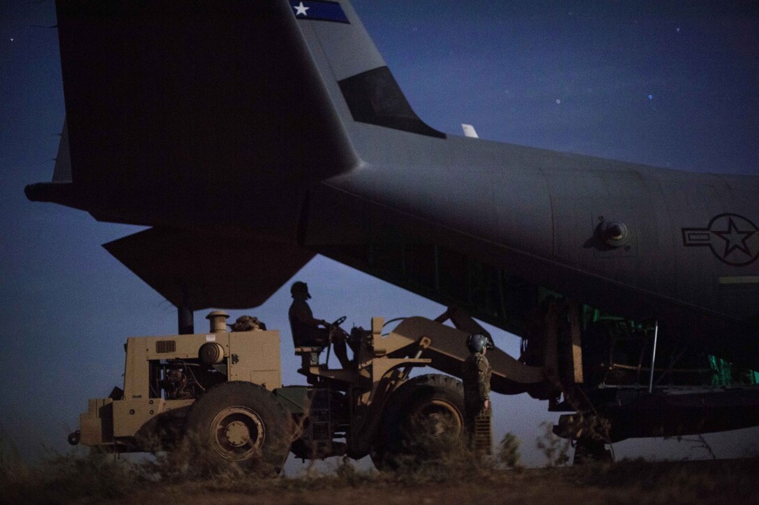 An airman uses a vehicle to load cargo into an aircraft.