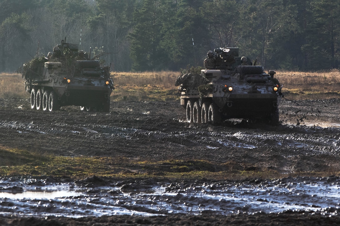 Soldiers maneuver twop Stryker vehicles into position through muddy terrain.