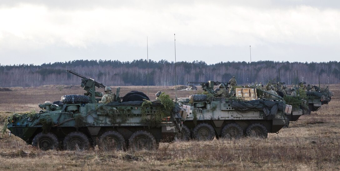 Soldiers drive Stryker vehicles into position in a field.