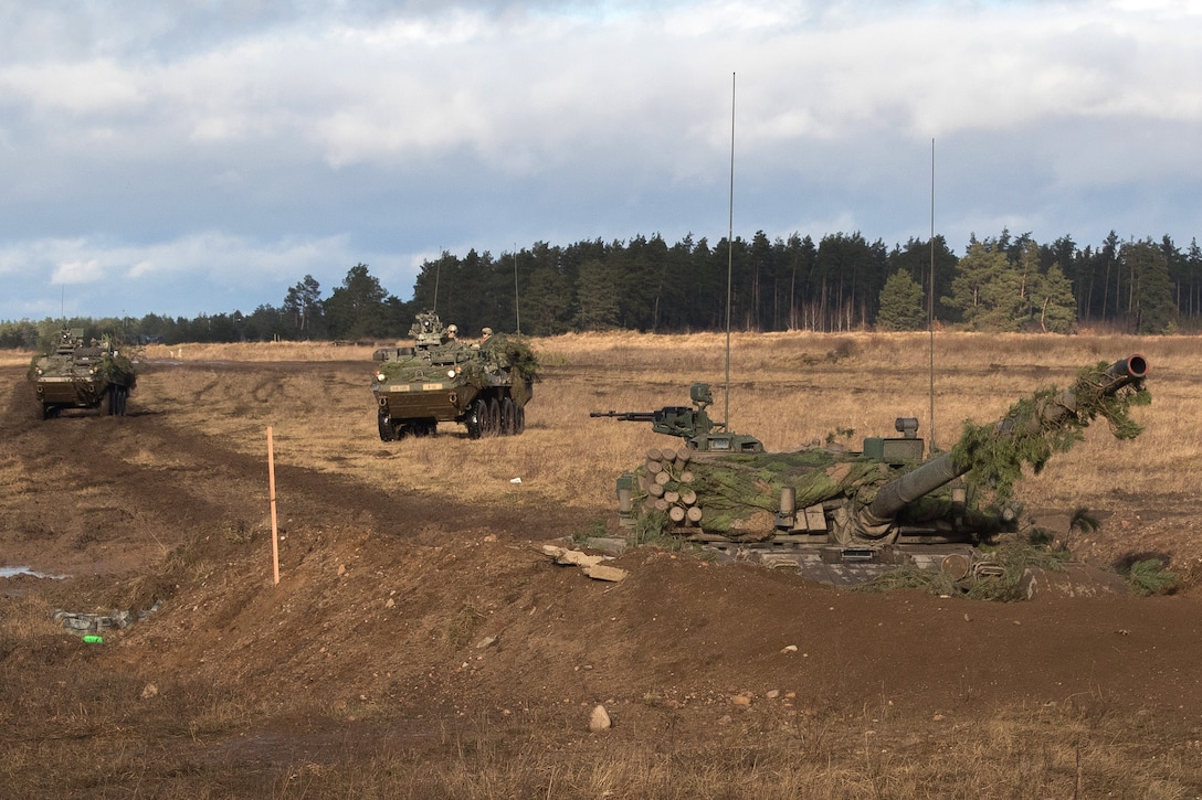 Two Stryker vehicles drive past a Polish tank.