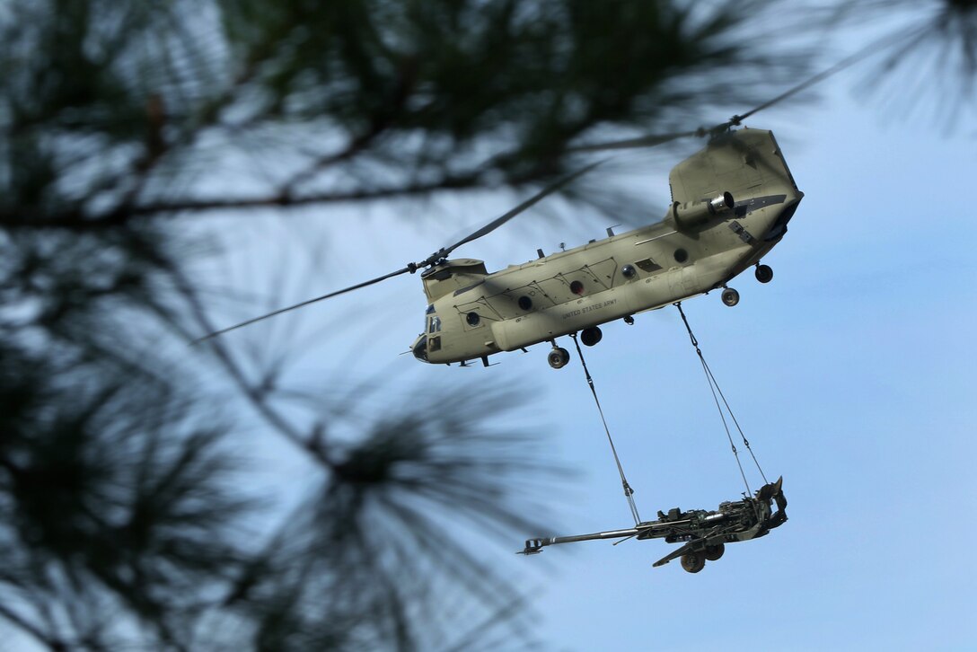 An Army helicopter sling loads a howitzer.