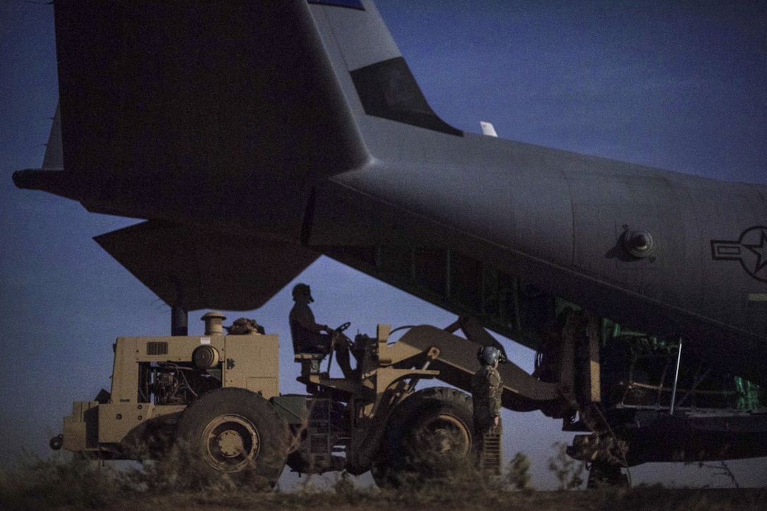 An airman drives a vehicle near an aircraft during cargo operations.