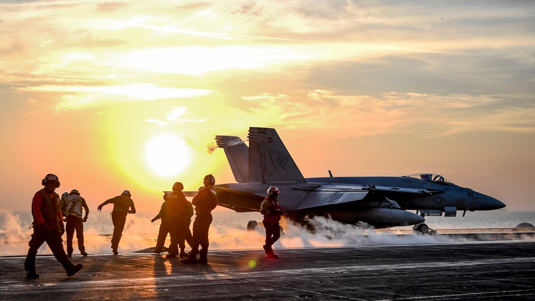 Sailors watch as an aircraft launches from a ship's flight deck.