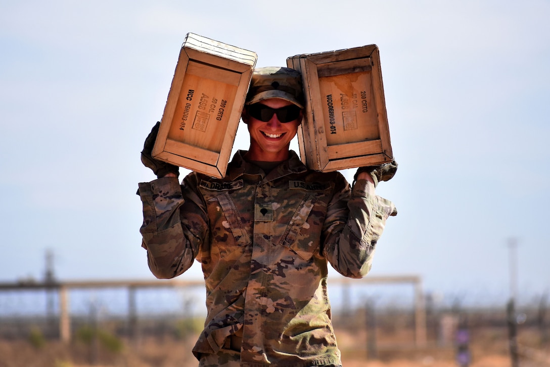 A soldier carries two cases of M9 blank ammunition on his shoulders..