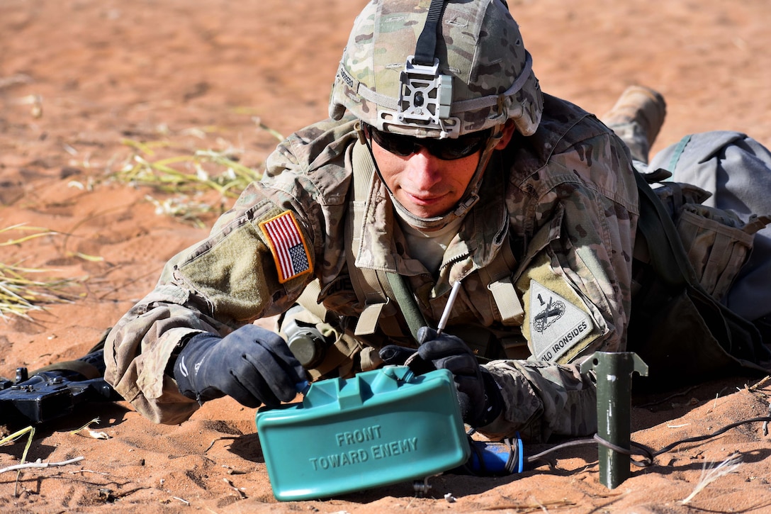 A soldier on the ground adjusts a blue mine.