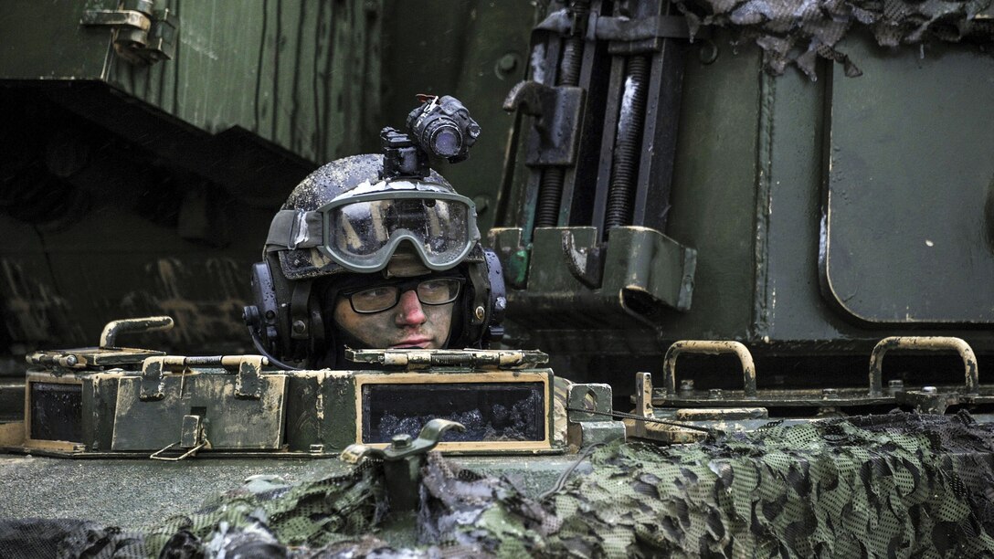 A soldier looks out from the driver's hatch of a howitzer.