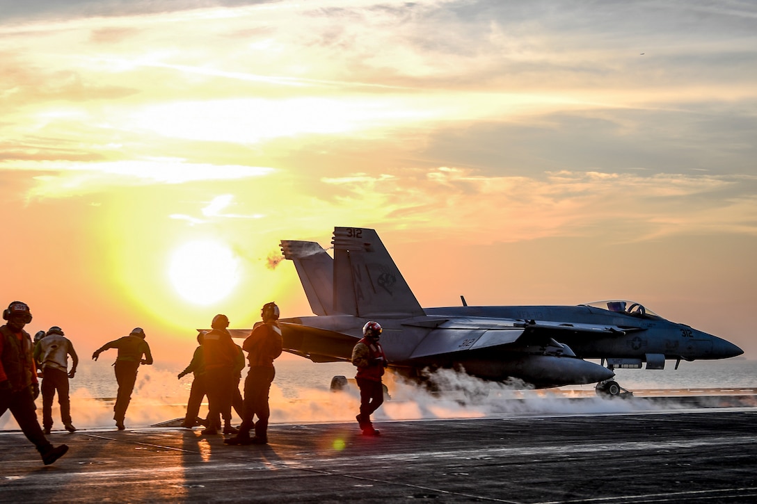 Sailors watch as an aircraft launches from a ship's flight deck.