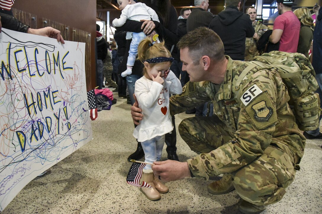 An airman prepares to hug his daughter as she places her hands over her eyes.