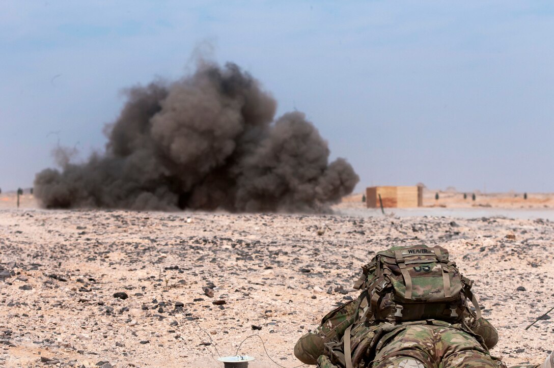 A soldier lays on the ground, far from an explosion.