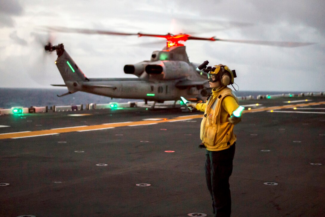 Navy Petty Officer 2nd Class Faith Phillips signals to the pilot of an AH-1Z Viper helicopter as it approaches the flight deck.