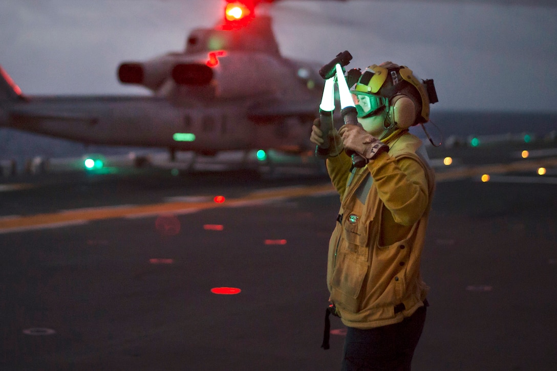 A sailor uses landing lights to signal a pilot.