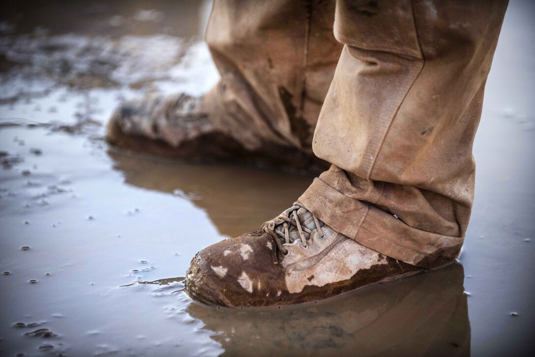 An airman stands in muddy water.