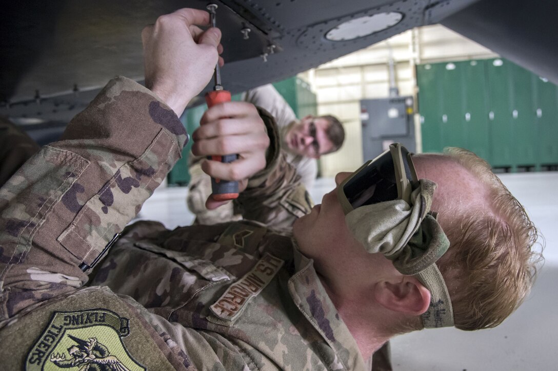 An airman secure bolts onto the bottom of a helicopter while laying on his back.