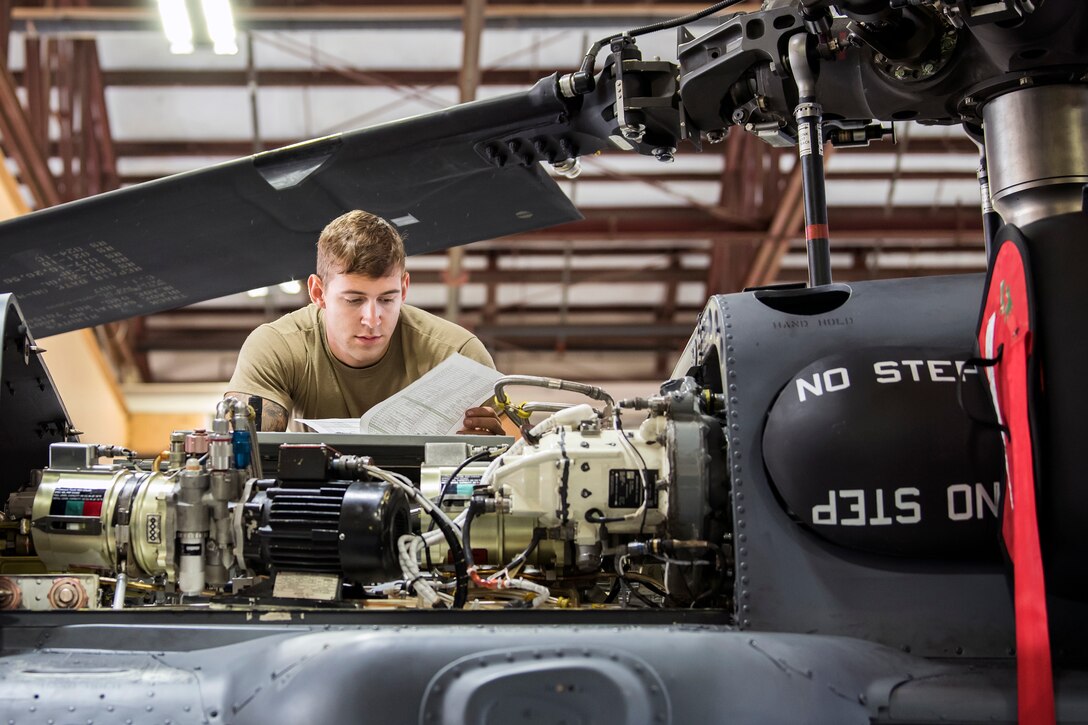 An airman reads paperwork while leaning on the top of a helicopter.