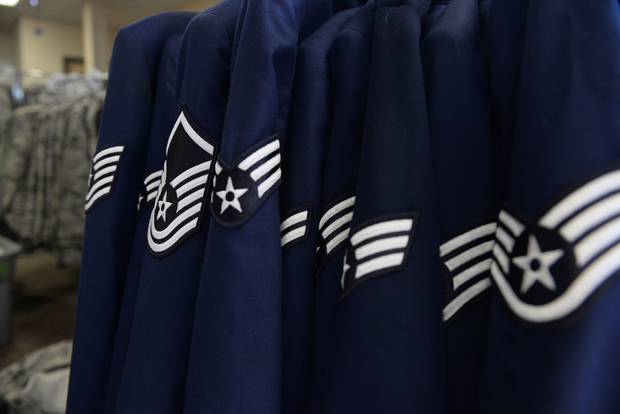 Air Force service jackets hung in a line with many different rank insignias including staff sergeant, senior airman, airman 1st class, master sergeant and technical sergeant.
