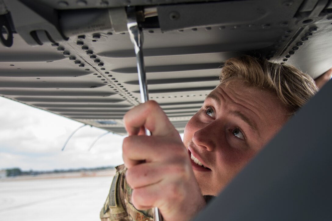 An airman tightens a bolt on the bottom of a helicopter.