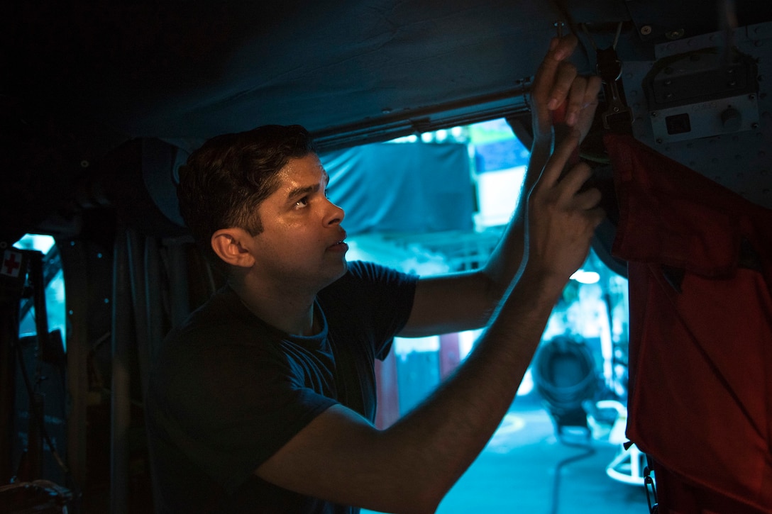 A sailor conducts maintenance inside of a helicopter.