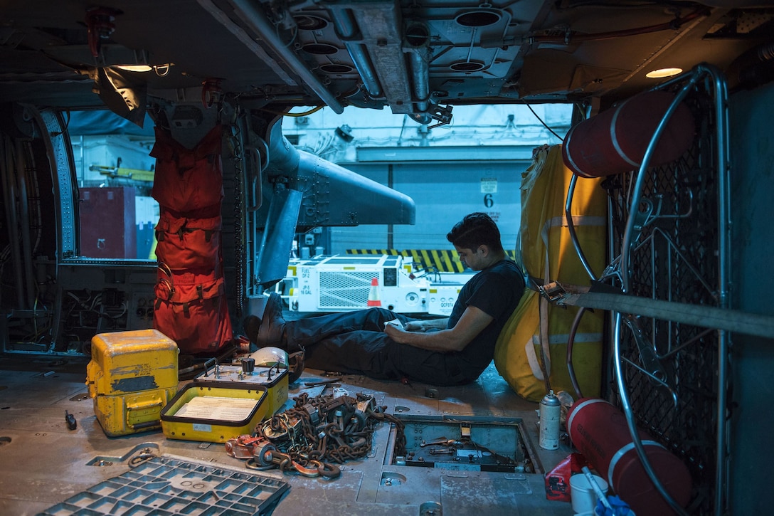 A sailor reviews a document while seated inside a helicopter.