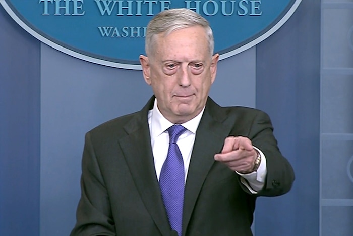 Defense Secretary James N. Mattis points while standing in front of a blue background and partially visible White House seal