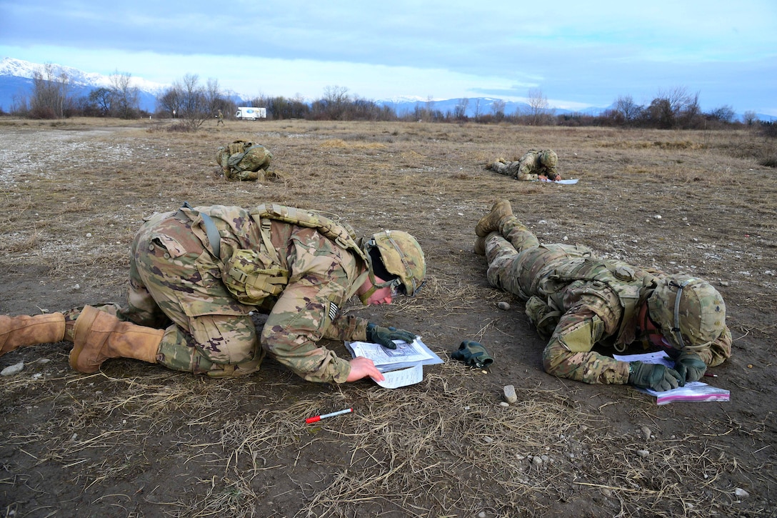Soldiers lay on the ground writing on papers.