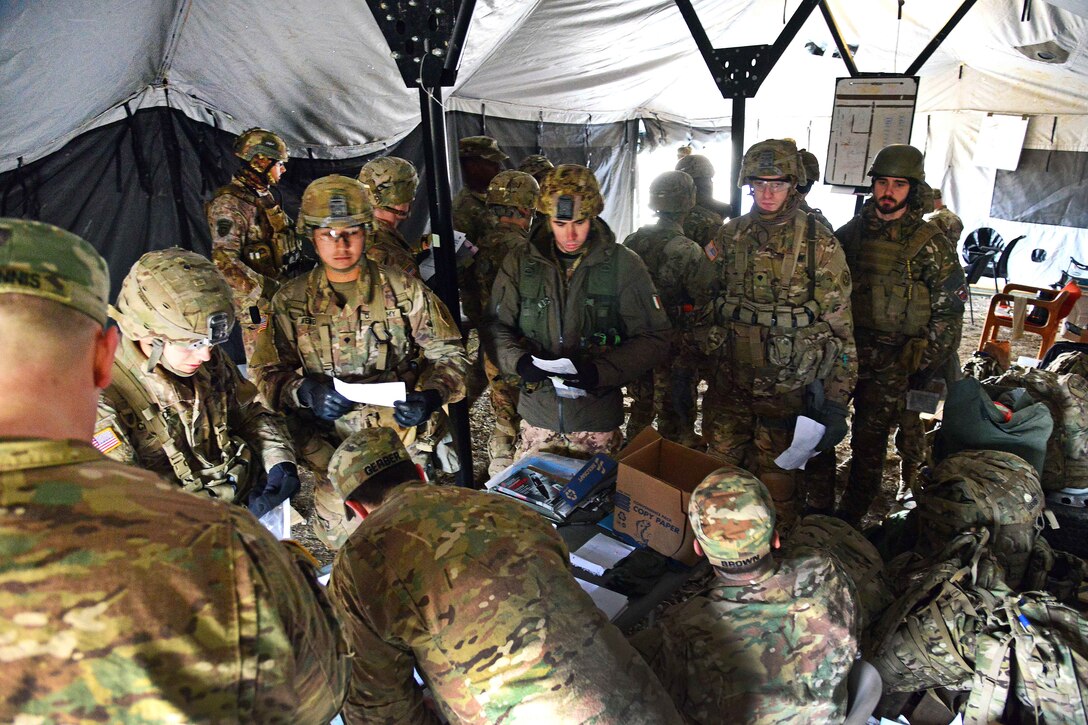 U.S. and Italian paratroopers sit and stand in a tent.