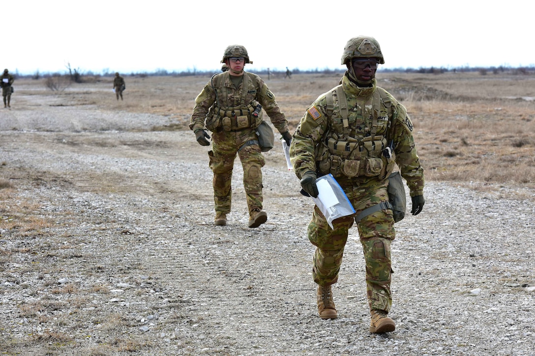 Soldiers walk along a gravel road.
