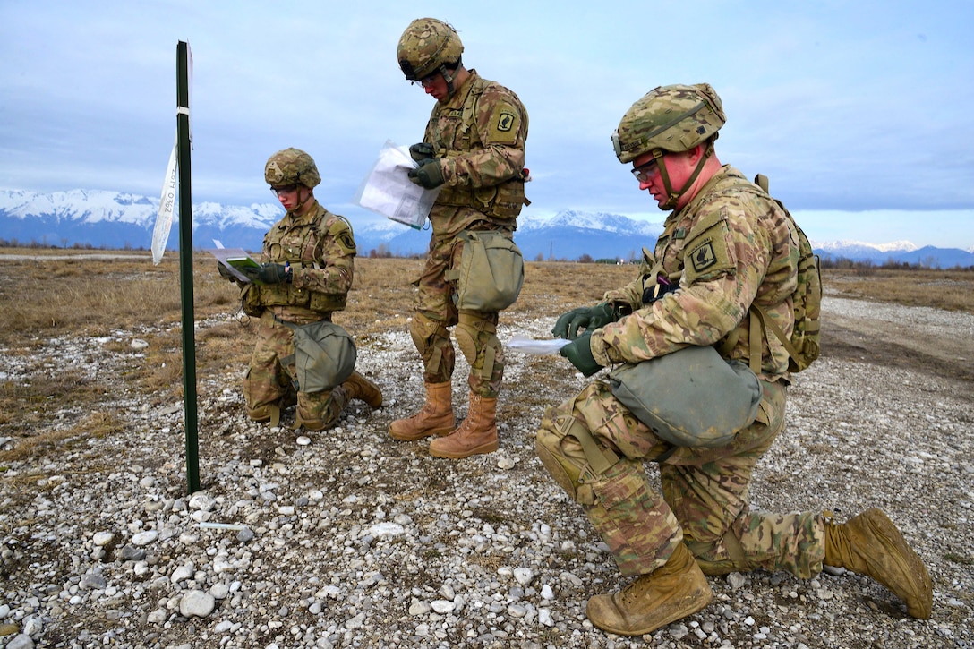 Two kneeling soldiers and one standing soldier write on papers.