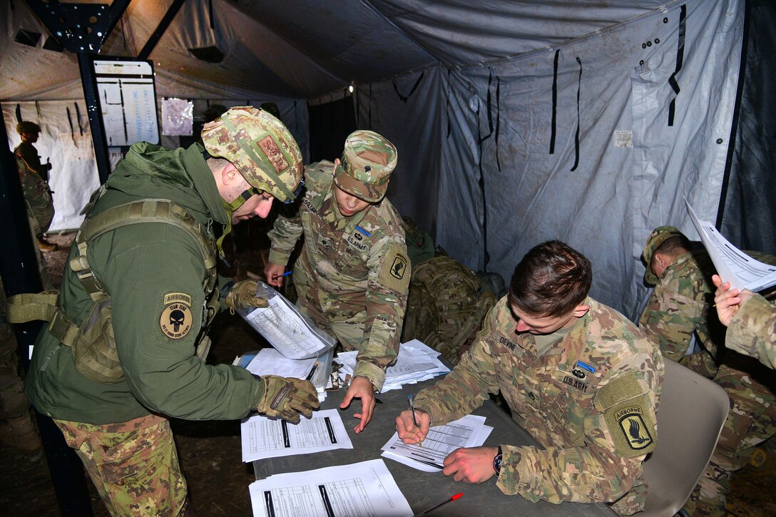 An Italian paratrooper turns in his results to an Italian soldier sitting at a table.