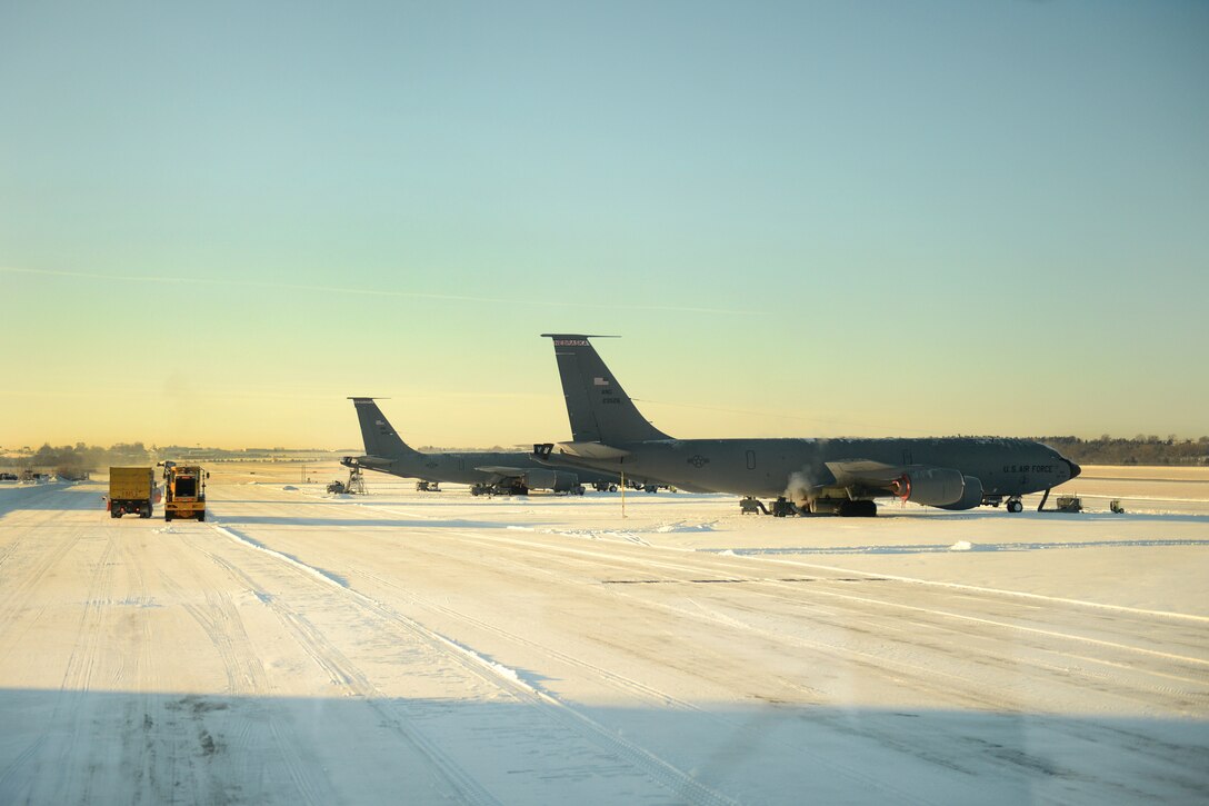 Air Force airmen and maintenance crews operate snow removal vehicles to clear snow off a flight line.