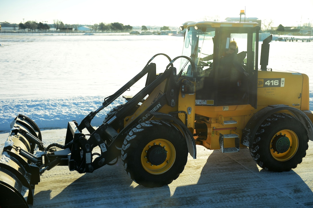 An Air Force airman operates a bulldozer to clear snow off a flight line.