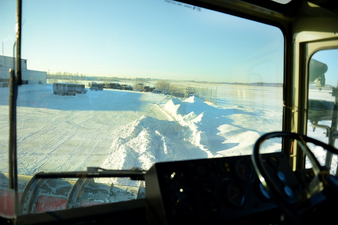 An Air Force airman operates heavy equipment vehicle to clear snow from a flight line.
