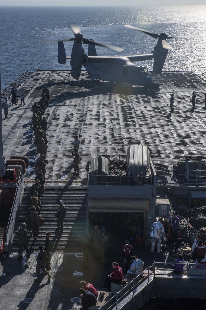 U.S. Marines and Japanese forces board an MV-22 Osprey tilt-rotor aircraft on the USS Rushmore flight deck.