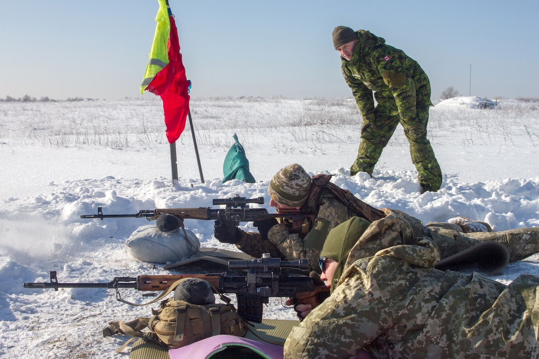 A Canadian soldier observes Ukrainian soldiers firing on a range.