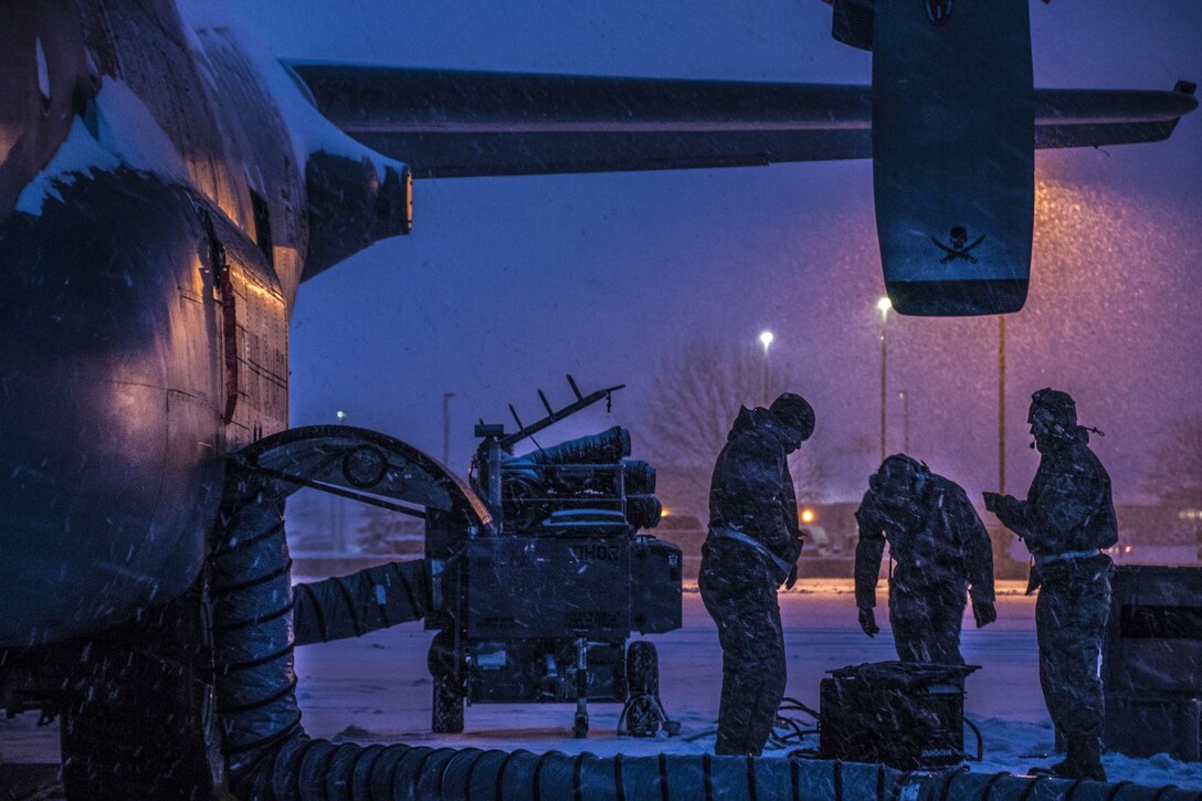 Airmen work on the brake systems of an aircraft during a snowstorm.