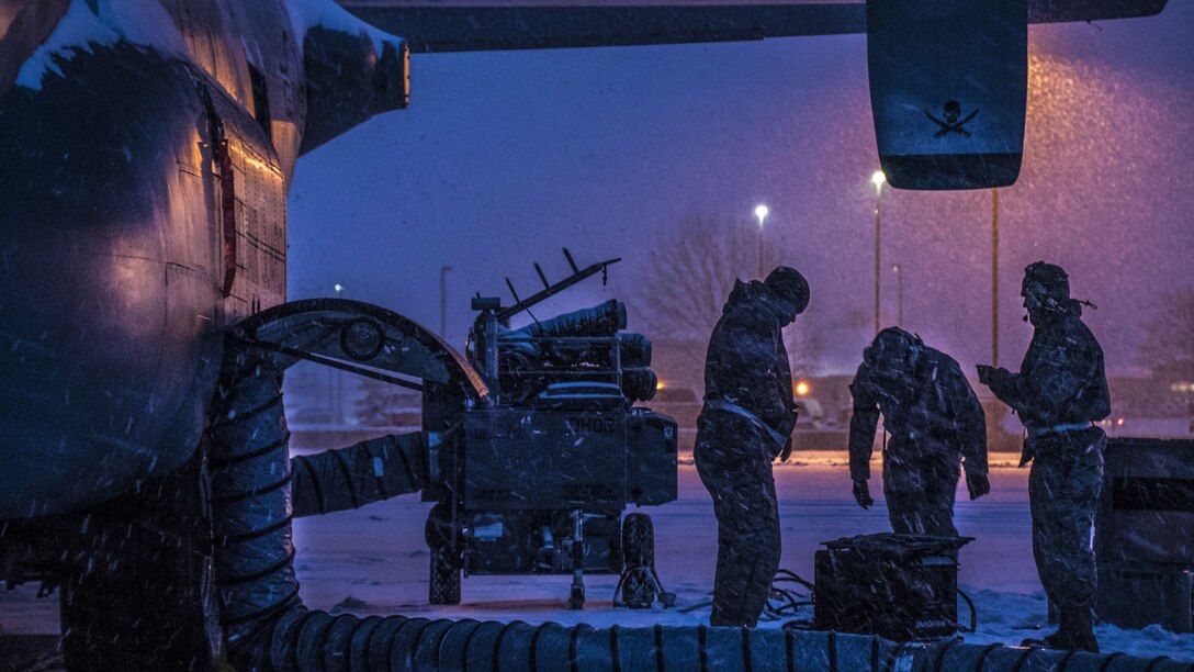 Airmen work on the brake systems of an aircraft during a snowstorm.