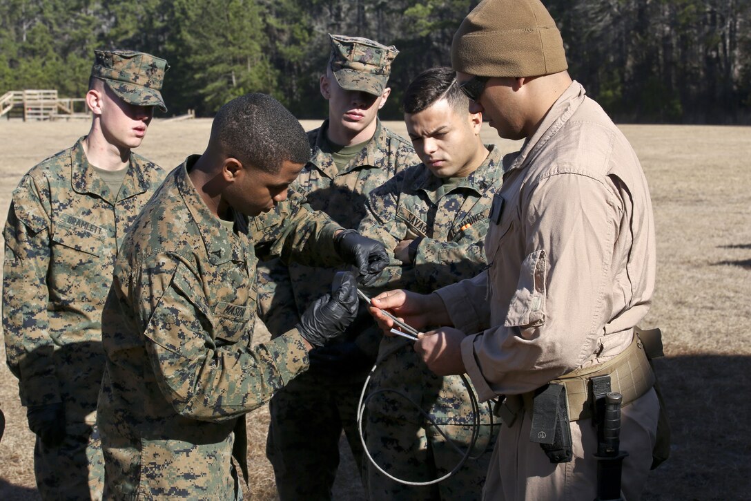 Four Marines watch as another Marine practices using a detonating cord.
