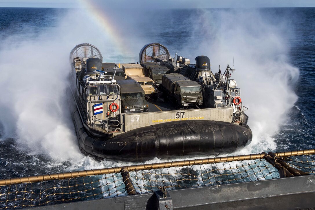 An air-cushioned landing craft approaches a ship as a rainbow forms over it.