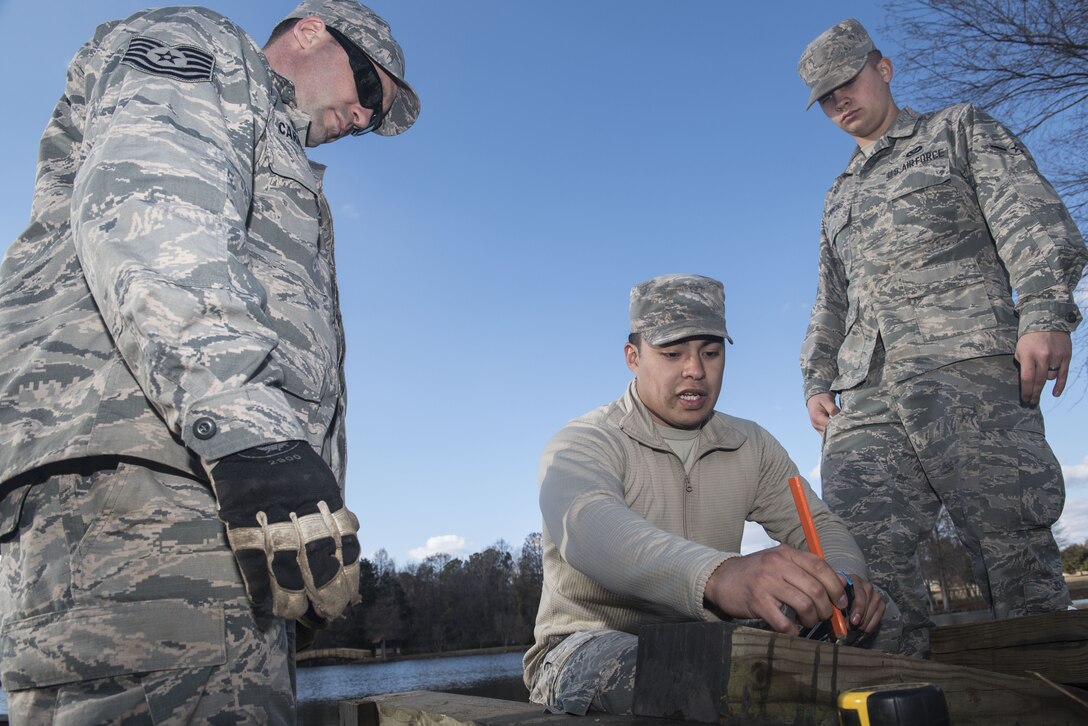 U.S. Air Force Tech. Sgt. Jeremy Carnahan, 20th Civil Engineer Squadron (CES) pavements and equipment journeyman, left, and Airman Zackery Simmons, 20th CES structural apprentice, right, listen as Senior Airman Daniel Nava, 20th CES structures journeyman, explains what cuts they need to make to begin building a bridge at Shaw Air Force Base, S.C., Feb. 5, 2018.