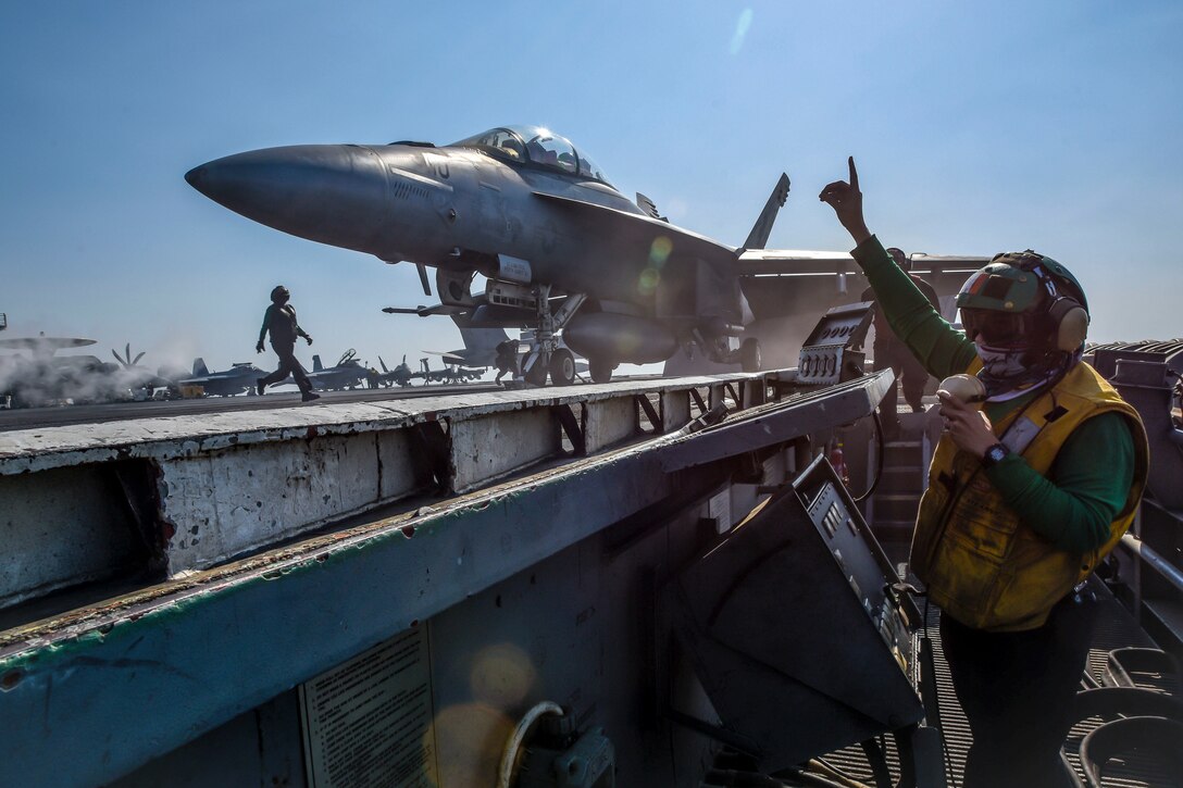 A sailor signals the upcoming launch of an aircraft from a ship.