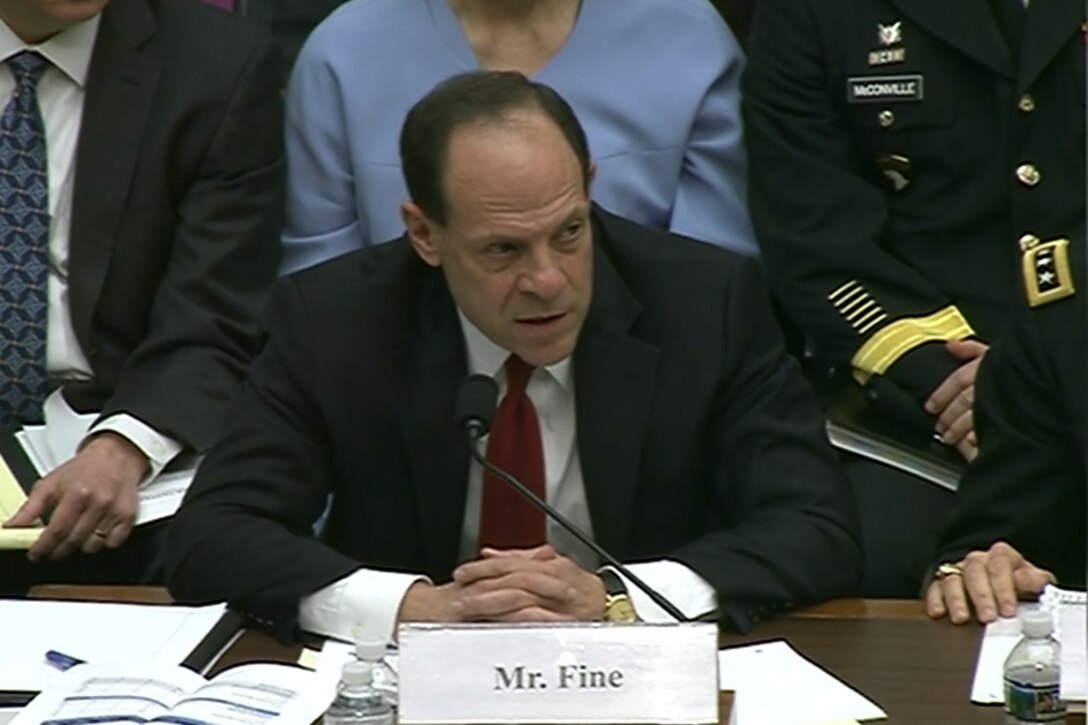 A Defense Department official sits behind a desk.