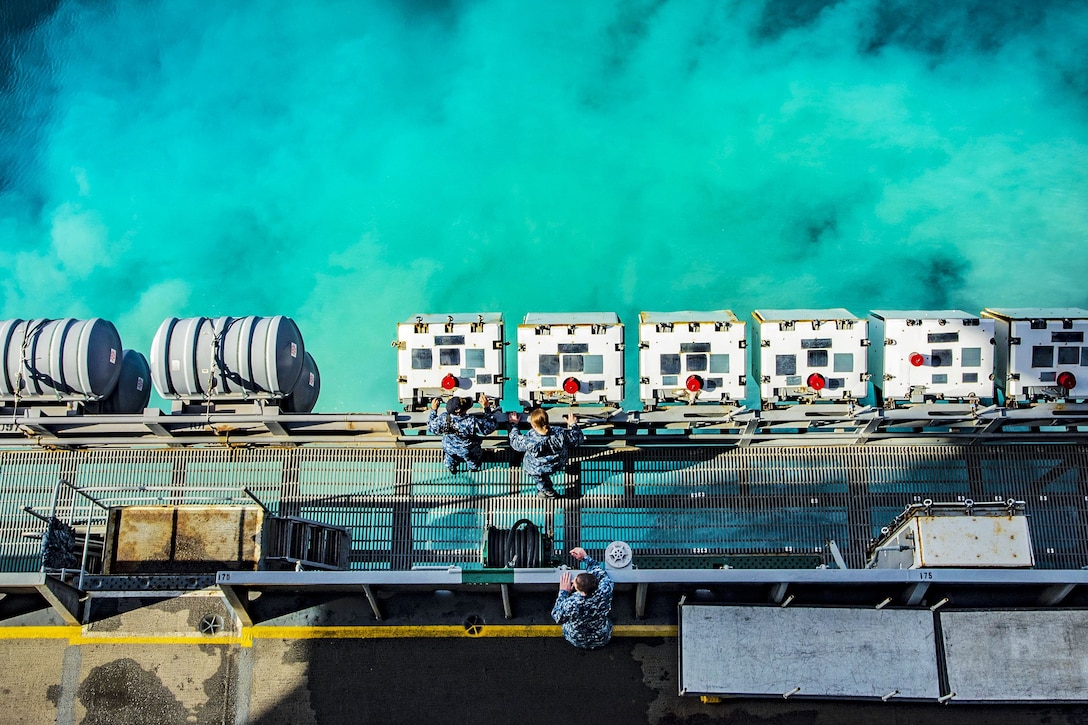 Sailors maintain ordnance lockers on a ship as it departs a port.