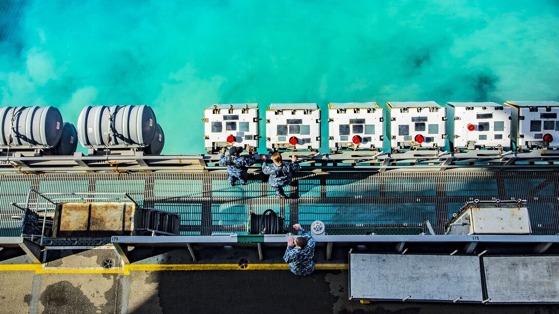 Sailors maintain ordnance lockers on a ship as it departs a port.