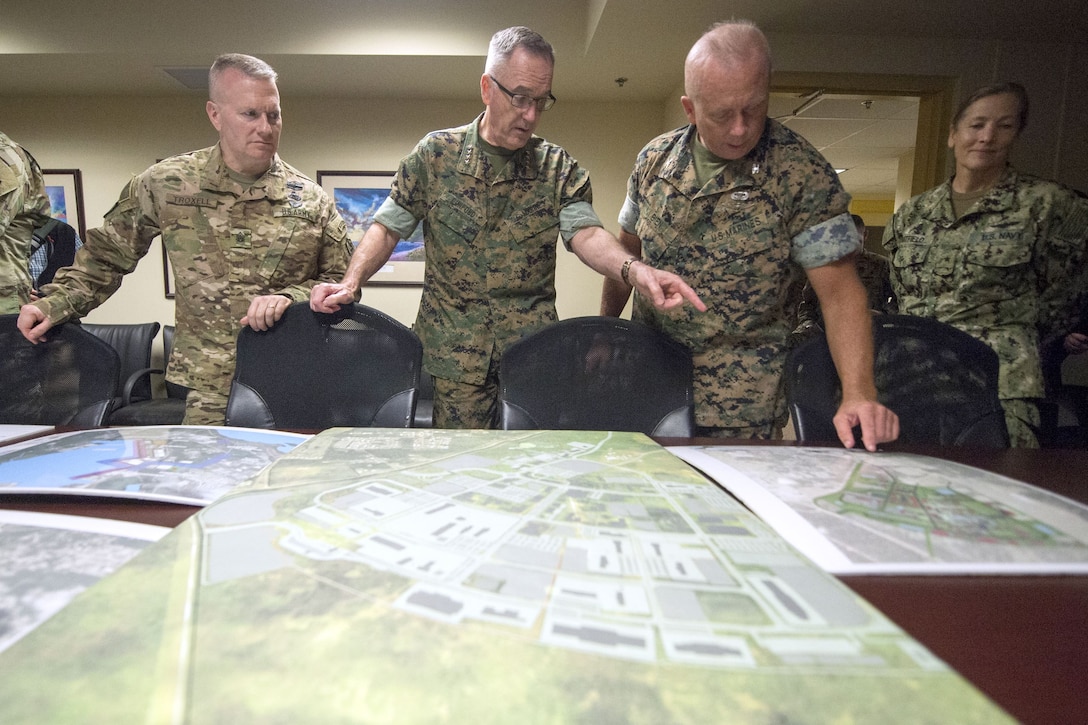 The chairman of the Joint Chiefs of Staff and other service members look at maps on a table.