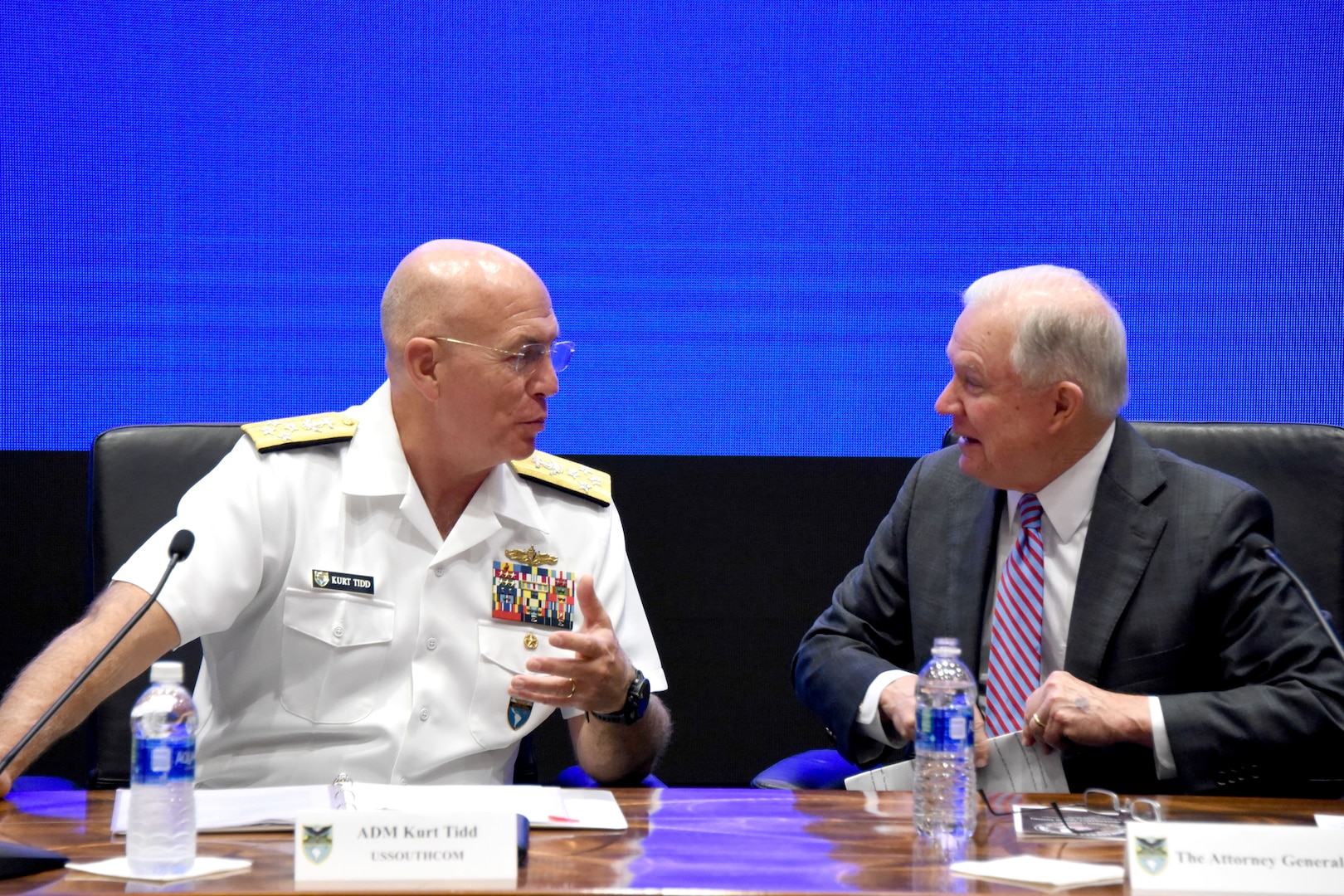 A Navy admiral and the attorney general talk while sitting behind a desk.