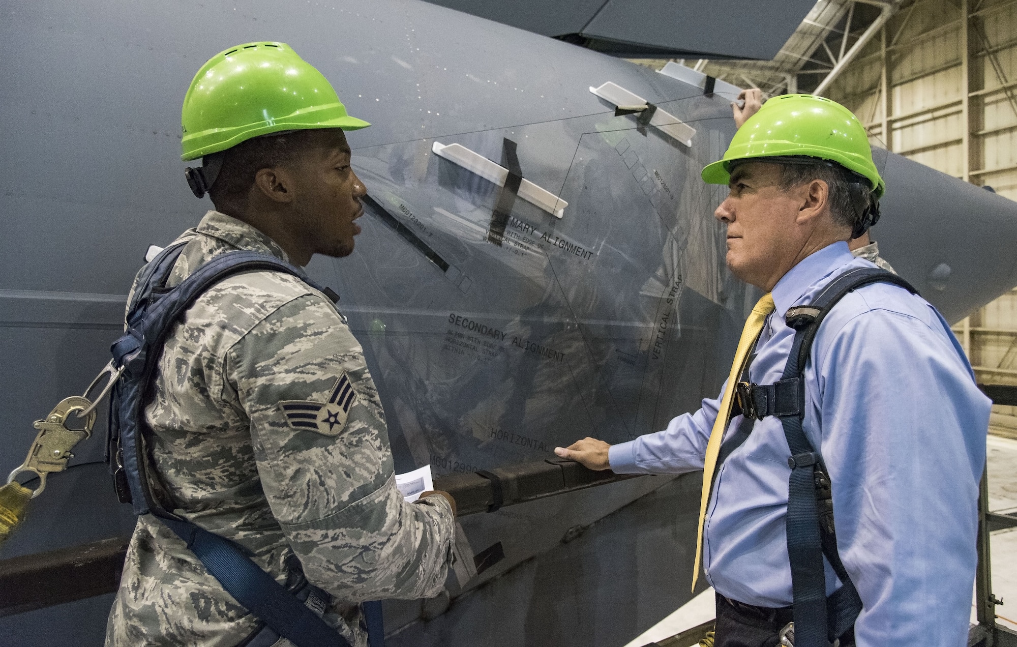Senior Airman Terrence Williamson, 736th Aircraft Maintenance Squadron aerospace maintenance journeyman, explains to Roberto Guerrero, Deputy Assistant Secretary of the Air Force for Operational Energy, Headquarters U.S. Air Force, Washington, D.C., how Microvanes positioned on each side at the rear of a C-17 Globemaster III fuselage using a Mylar template, Sept. 6, 2017, at Dover Air Force Base, Del. Microvanes essentially clean up the airflow in the region of the cargo door by re-energizing the air with small vortices that delay separation, smooth the flow, and reduce drag. “The programs APTO is working on are great examples of how we can increase our combat capability through the smart use of operational energy,” said Guerrero. (U.S. Air Force photo by Roland Balik)