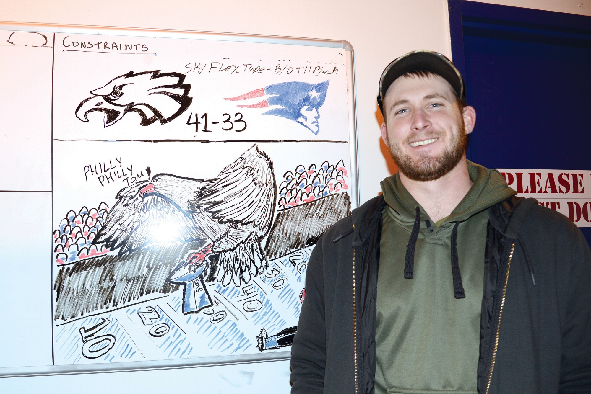 Kody Kolke, a hazardous material handler with the 565th Aircraft Maintenance Squadron, takes a few minutes out of his work day to help boost morale by drawing funny or patriotic scenes on a whiteboard in a heavily-travelled hallway in Bldg. 2121.