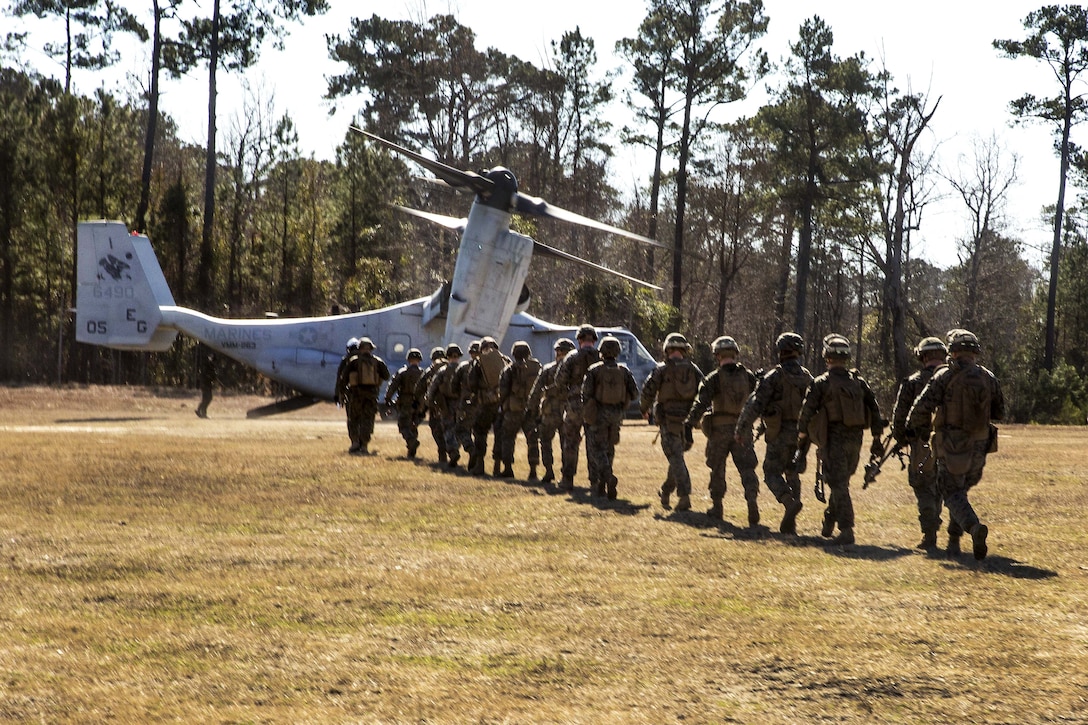 Marines and sailors form a line to board an MV-22 Osprey aircraft.