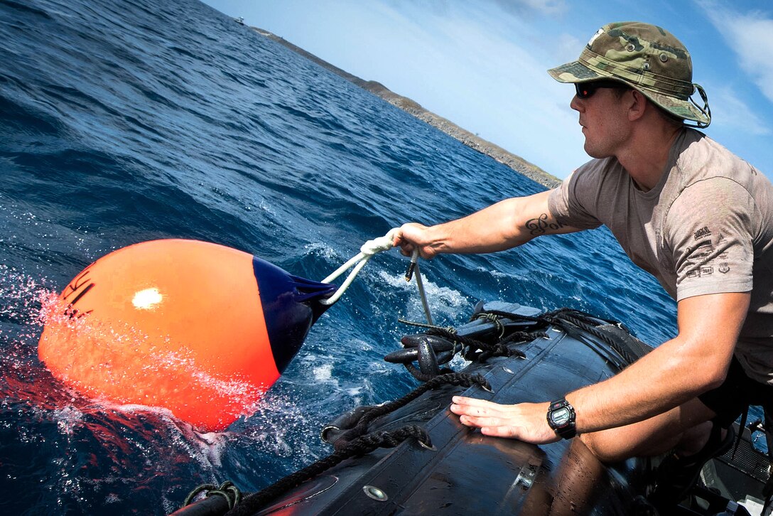 A sailor drops an orange buoy off the side of a boat.
