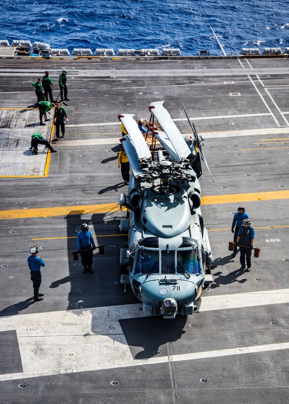 Sailors move a Seahawk helicopter on a flight deck.
